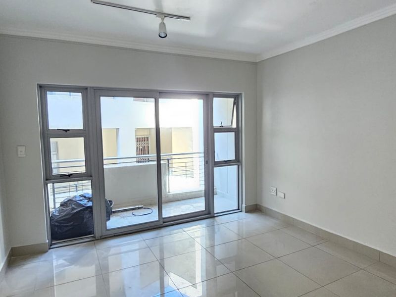 An empty living room featuring neutral tiled flooring, cove cornicing, and a large sliding glass door providing access to a balcony.