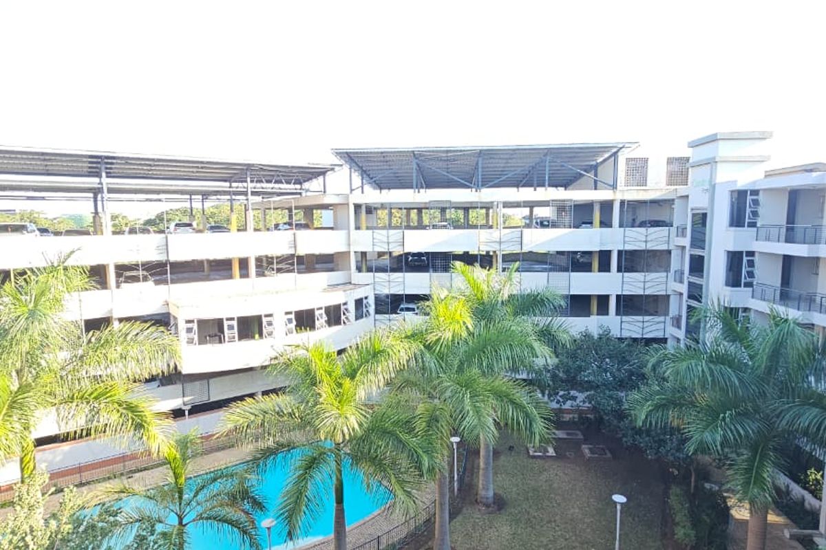 Aerial view of an apartment complex featuring a swimming pool, landscaped garden, and a multi-level parking structure.