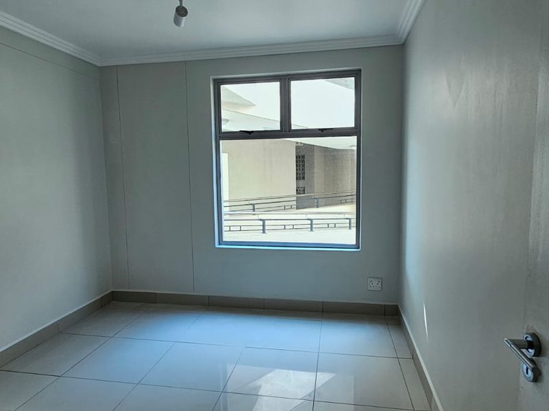 A clean, empty bedroom featuring neutral tiled flooring, smooth walls, and a large window providing natural light.
