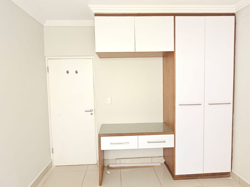 A clean bedroom featuring built-in white and wood-tone cabinetry, including a wardrobe and integrated desk area with tiled flooring.