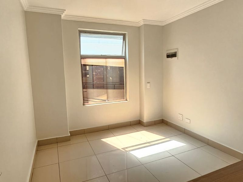 A bright, empty bedroom featuring neutral walls, tiled flooring, and a window allowing natural light, providing a clean canvas for personalization.