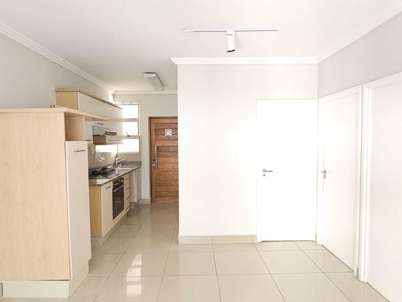 An open-plan living area featuring tiled flooring, neutral walls, and a functional kitchen with built-in cabinetry, oven, and hob.