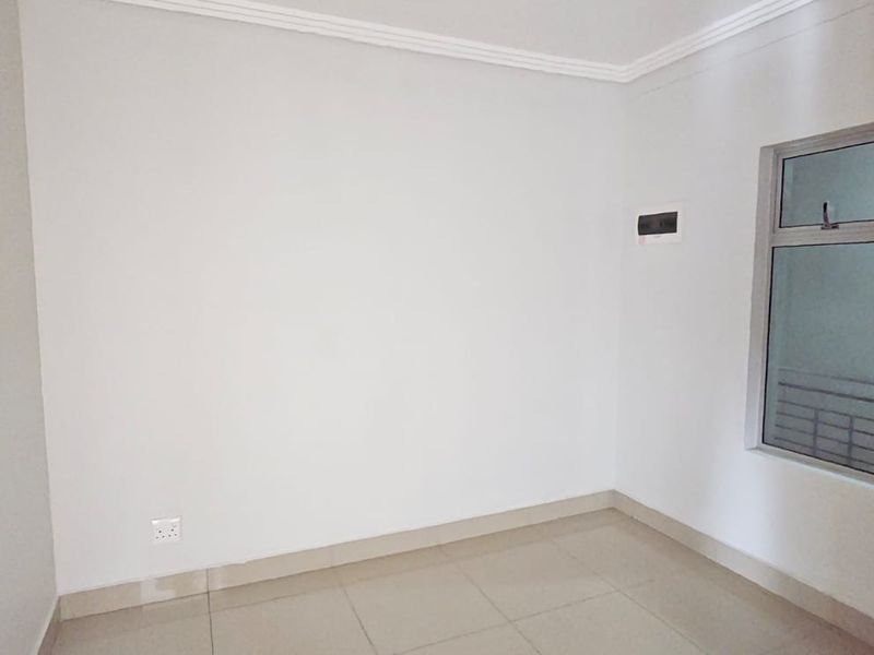 A clean, empty bedroom featuring neutral tiled flooring, white walls, and an aluminium-framed window, providing a blank canvas for interior design.