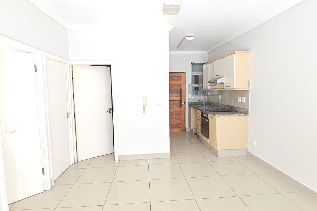 An open-plan living area featuring a compact kitchen with built-in cabinetry, granite countertops, and tiled flooring throughout.