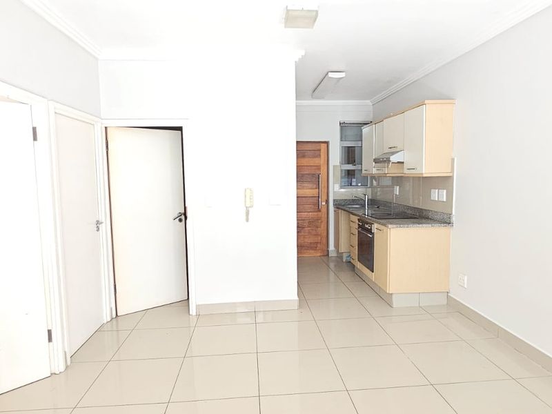 An open-plan living area featuring a compact kitchen with built-in cabinetry, granite countertops, and tiled flooring throughout.