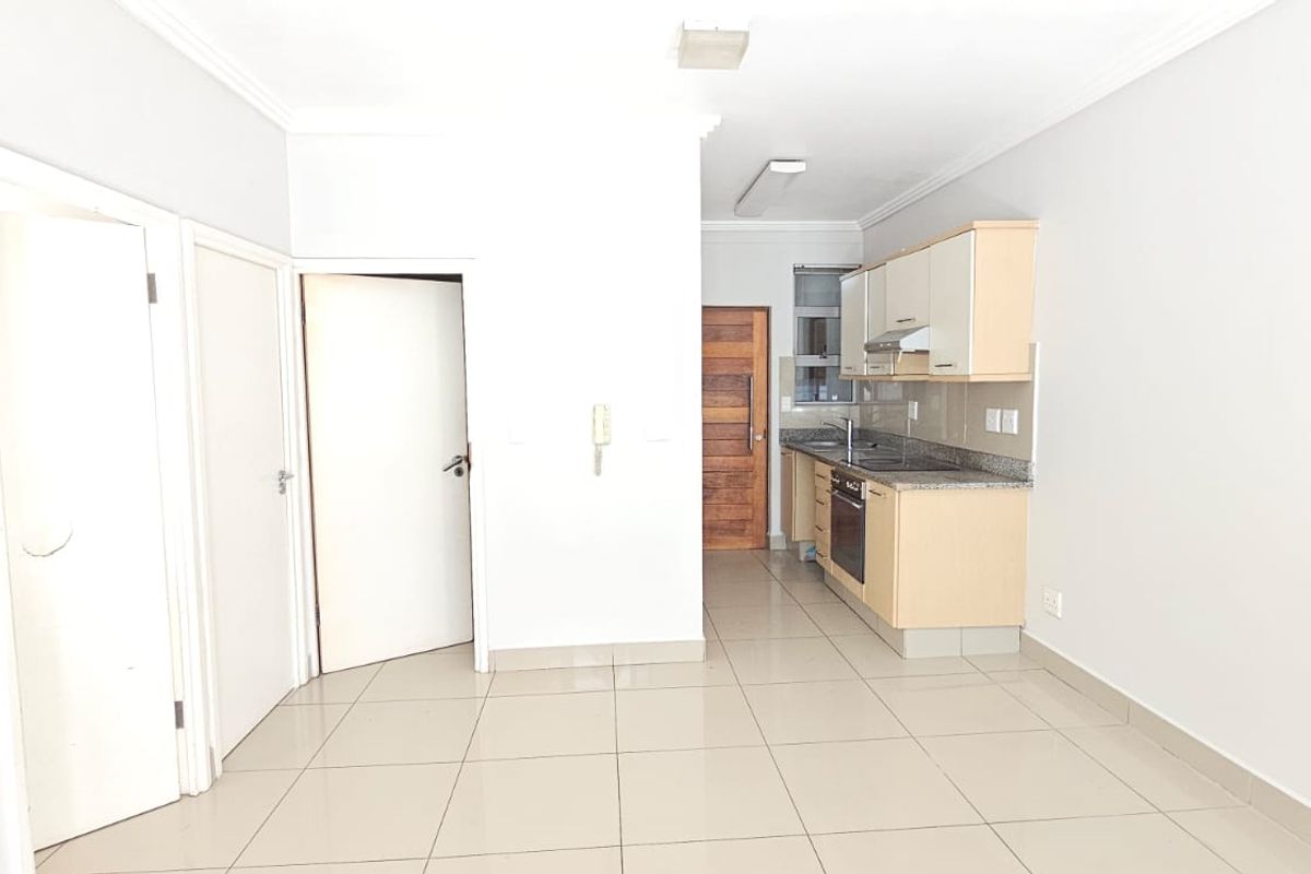 An open-plan living area featuring tiled flooring and a compact kitchen with built-in cabinetry, granite countertops, and integrated oven and extractor fan.