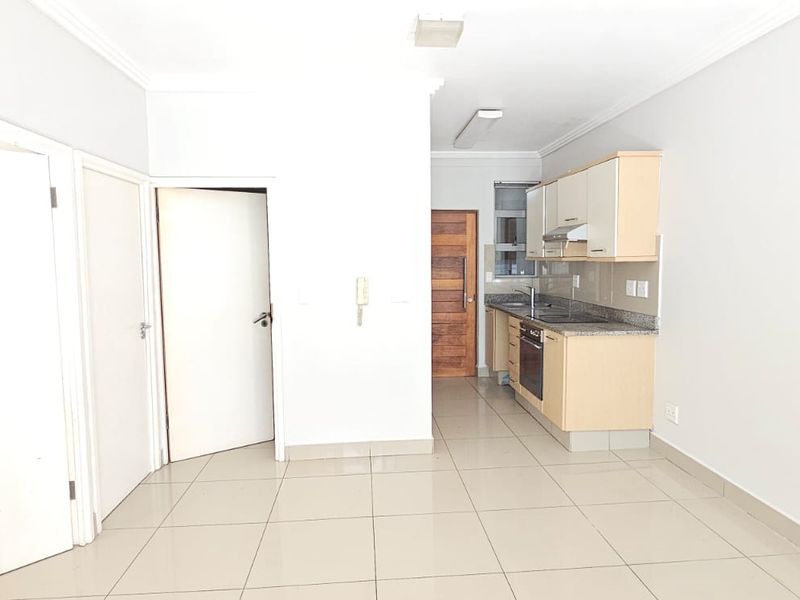 An open-plan living area featuring tiled flooring and a compact kitchen with built-in cabinetry, granite countertops, and integrated oven and extractor fan.
