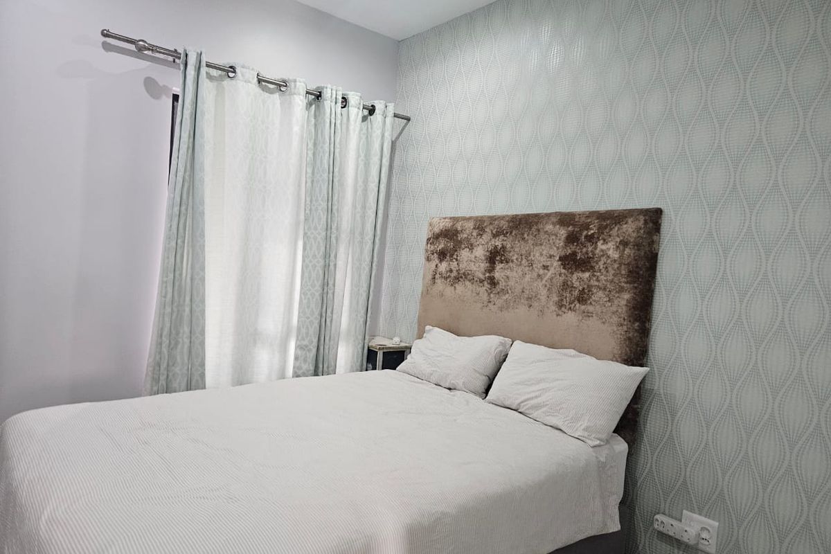 A well-maintained bedroom featuring patterned wallpaper, a curtain rod, and a functional electrical outlet.