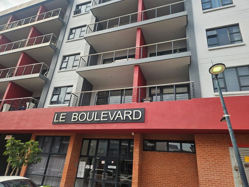 Front exterior view of Le Boulevard apartment complex, featuring a modern brick and concrete facade with multiple balconies and secure entrance.