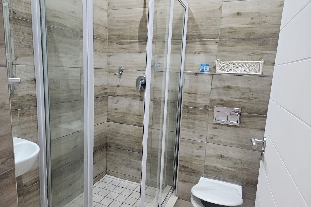 Modern bathroom featuring a glass shower enclosure, wall-mounted toilet with concealed cistern, and contemporary wood-look ceramic wall tiling.
