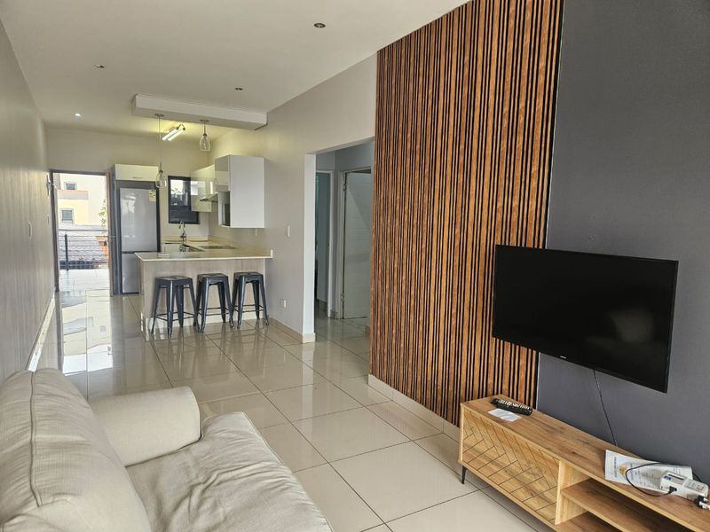 Open-plan living area featuring tiled floors, a modern kitchen with island, and a decorative wood-slat feature wall.