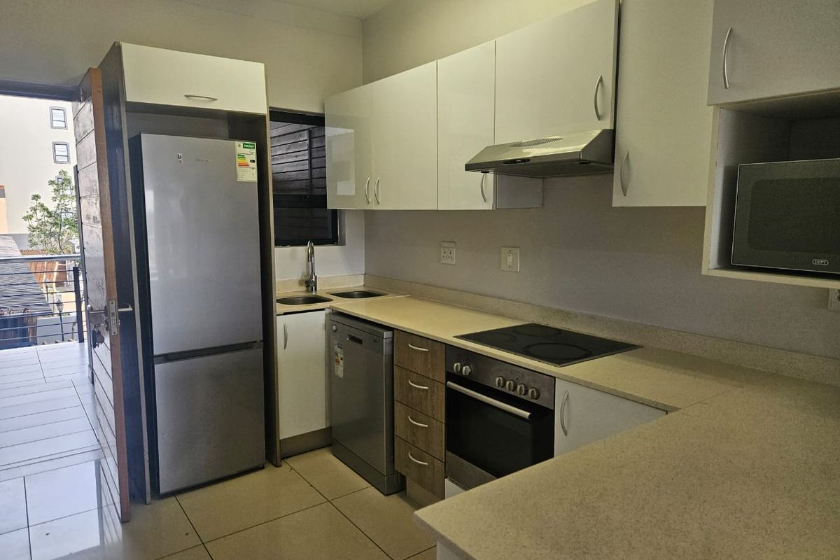 Modern kitchen featuring white cabinetry, stone countertops, integrated electric hob, oven, extractor fan, and tiled flooring with direct access to a balcony.