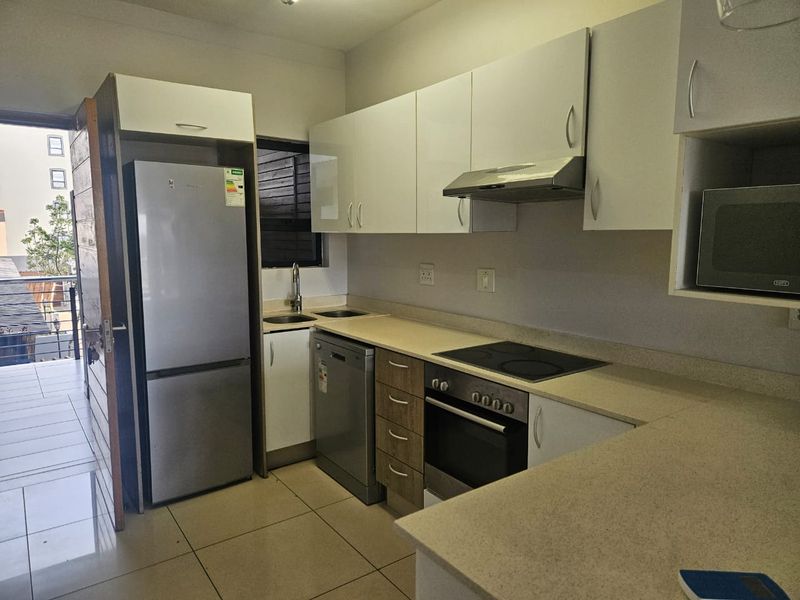Modern kitchen featuring white cabinetry, stone countertops, integrated electric hob, oven, extractor fan, and tiled flooring with direct access to a balcony.