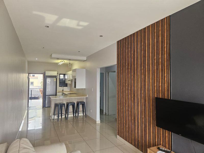 Modern open-plan living area featuring a sleek kitchen with island, tiled floors, and a contemporary timber slat feature wall.