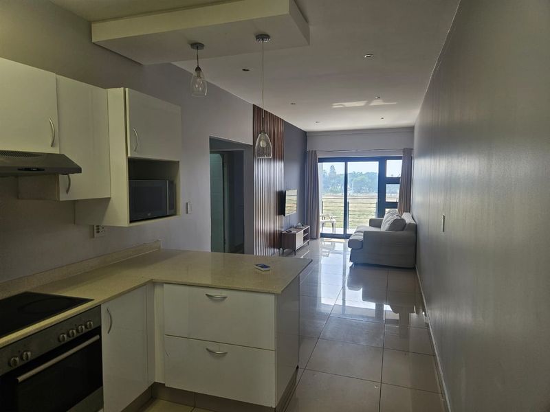 Modern open-plan living area featuring a sleek kitchen with stone countertops, integrated appliances, tiled floors, and direct access to a balcony with scenic views.