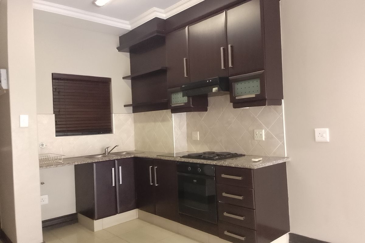 A functional kitchen featuring dark wood cabinetry, granite countertops, a built-in oven with gas hob, and a tiled backsplash.