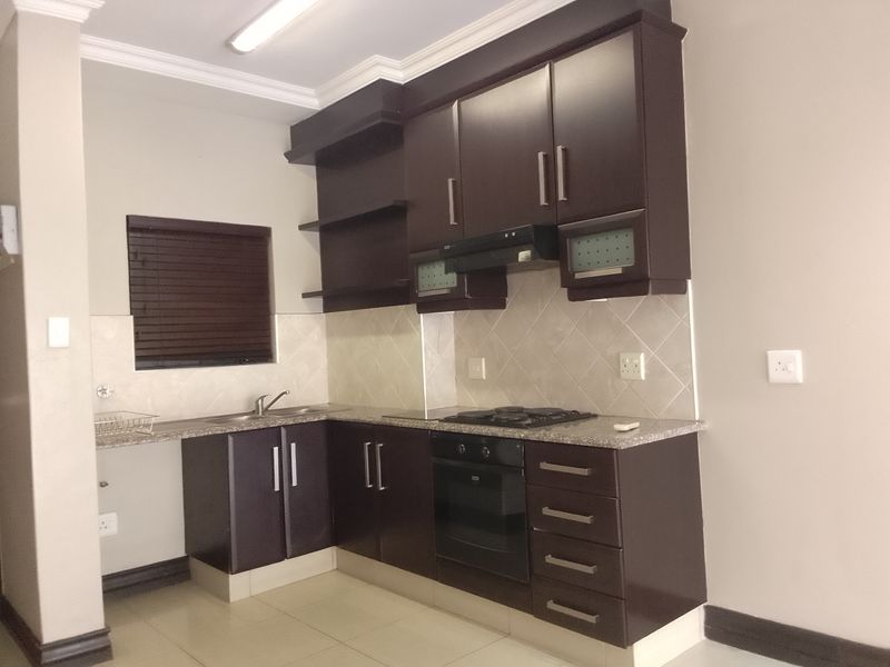 A functional kitchen featuring dark wood cabinetry, granite countertops, a built-in oven with gas hob, and a tiled backsplash.