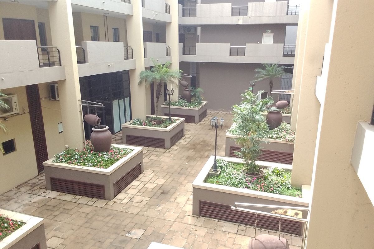 A well-maintained apartment complex courtyard featuring paved walkways, raised garden beds with integrated water features, and multi-level balcony access.