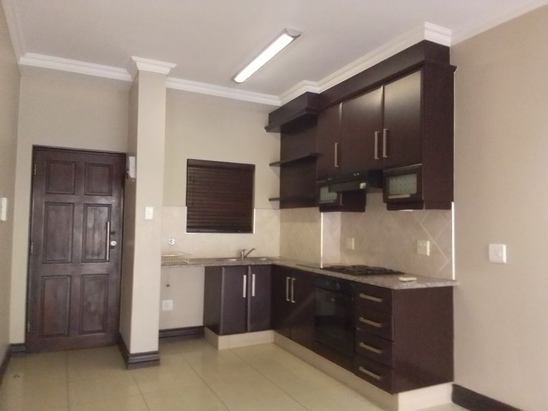 A functional kitchen featuring dark wood cabinetry, granite countertops, built-in oven, gas hob, and tiled flooring in an open-plan layout.