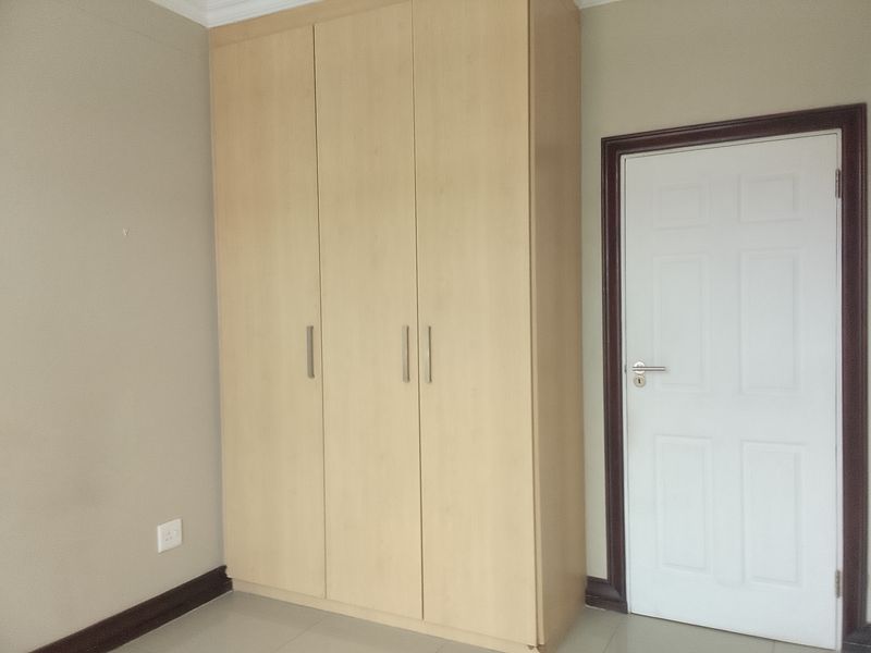 A clean, empty bedroom featuring a light wood-finish built-in wardrobe, tiled flooring, and neutral wall tones.
