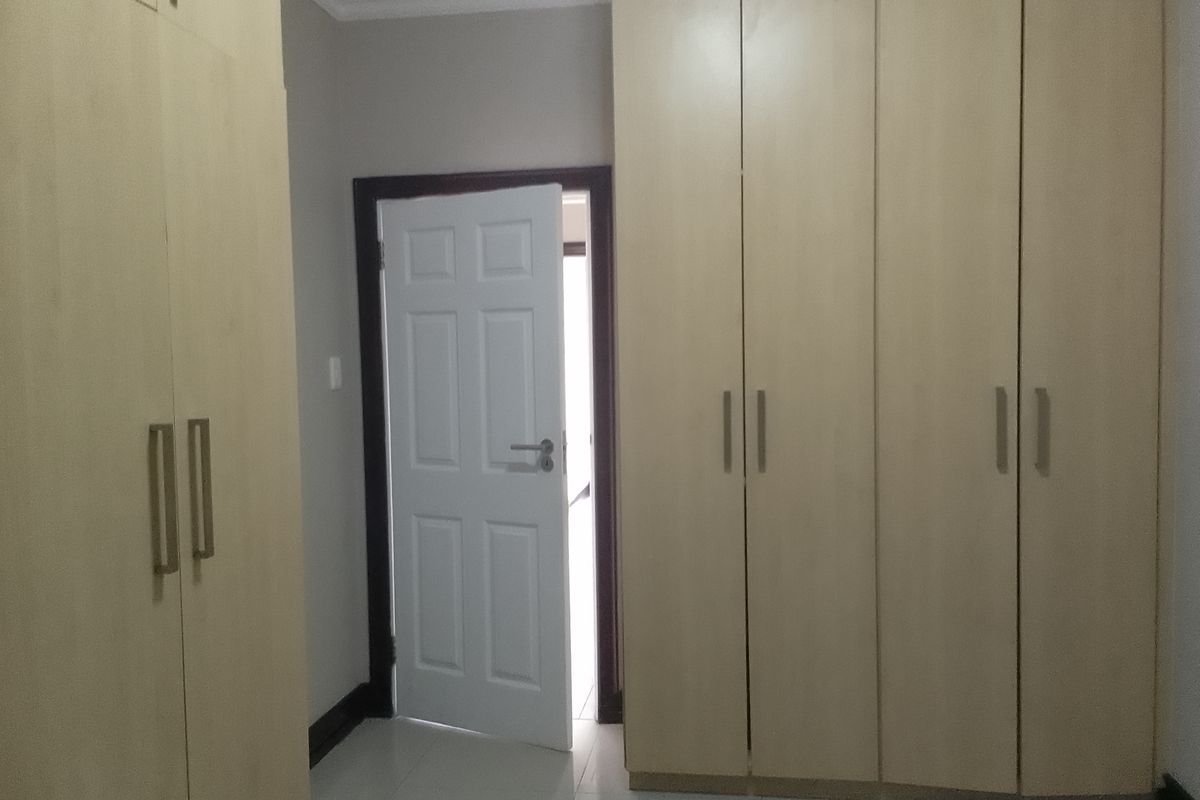 A bedroom featuring light wood-finish built-in cupboards, tiled flooring, and a white panel door leading to an adjacent space.