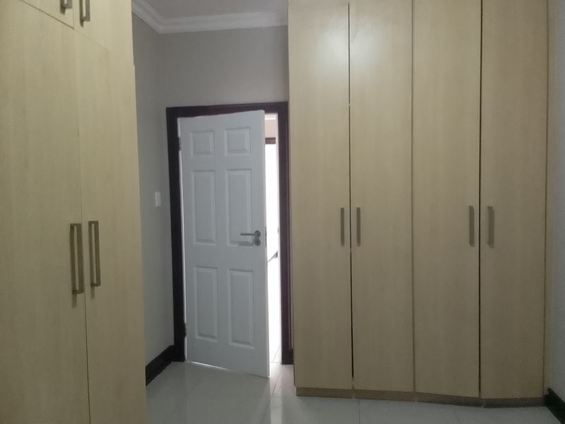 A bedroom featuring light wood-finish built-in cupboards, tiled flooring, and a white panel door leading to an adjacent space.