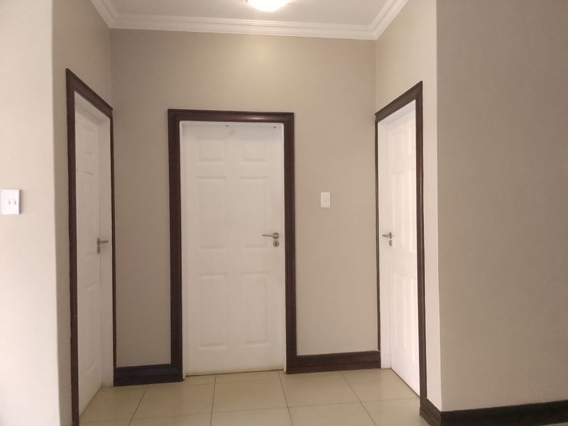 A clean and well-maintained hallway featuring neutral wall tones, tiled flooring, and multiple internal doors with dark wood-look frames.