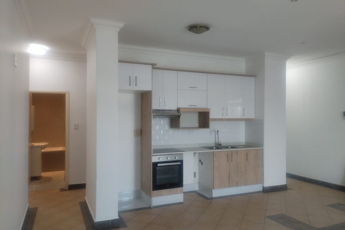 Open plan kitchen area featuring modern two-tone cabinetry, built-in oven and hob, and tiled flooring, with an adjacent view into the bathroom.
