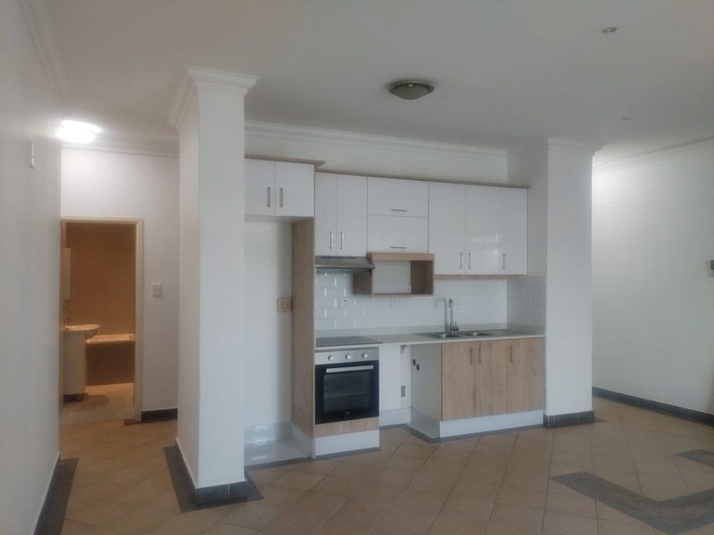 Open plan kitchen area featuring modern two-tone cabinetry, built-in oven and hob, and tiled flooring, with an adjacent view into the bathroom.