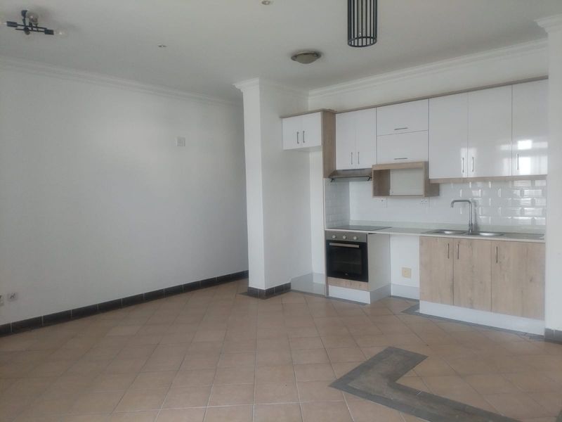Open plan living area featuring a modern kitchen with built-in cabinetry, electric hob, oven, and tiled flooring throughout.