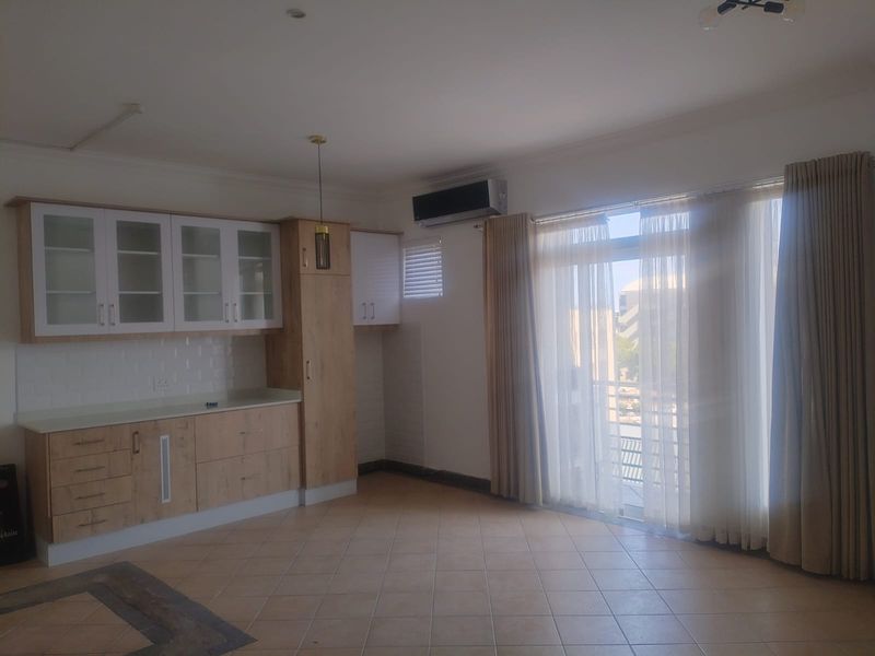 An open-plan living and kitchen area featuring light wood cabinetry, tiled flooring, and a sliding glass door leading to a balcony.