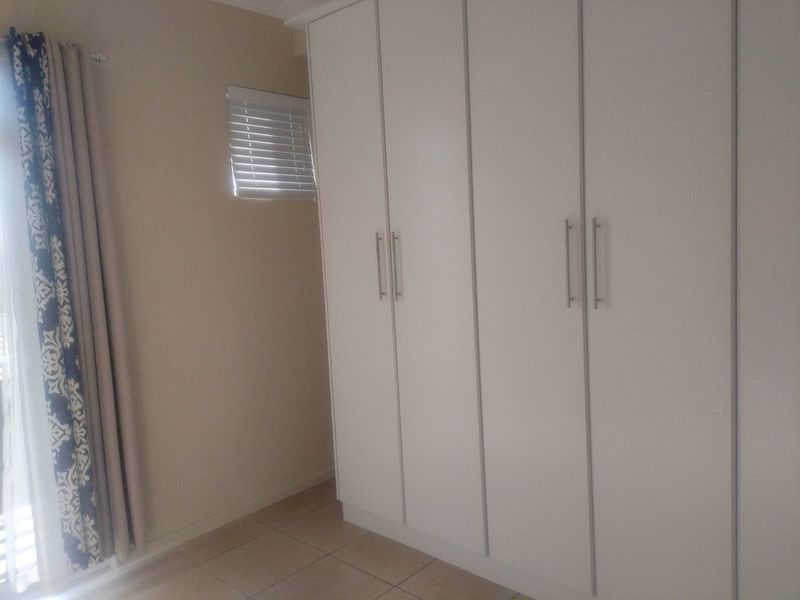 A clean bedroom featuring neutral tiled flooring and ample built-in cupboard storage with modern handles.