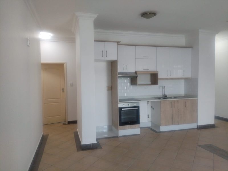 A compact kitchen featuring white and wood-tone cabinetry, built-in oven and hob, tiled backsplash, and tiled flooring in an open-plan layout.