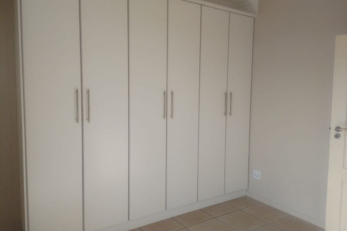A clean, empty bedroom featuring neutral-toned tiled flooring and extensive floor-to-ceiling built-in cupboards with modern hardware.