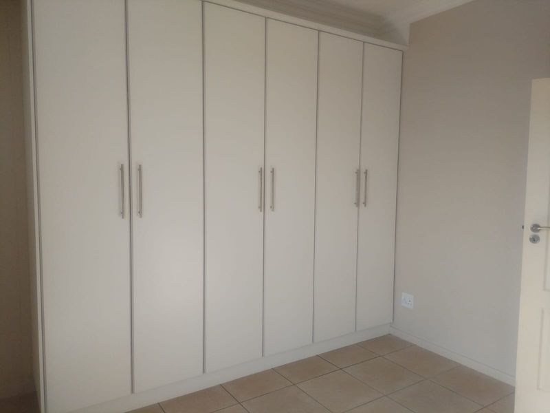A clean, empty bedroom featuring neutral-toned tiled flooring and extensive floor-to-ceiling built-in cupboards with modern hardware.