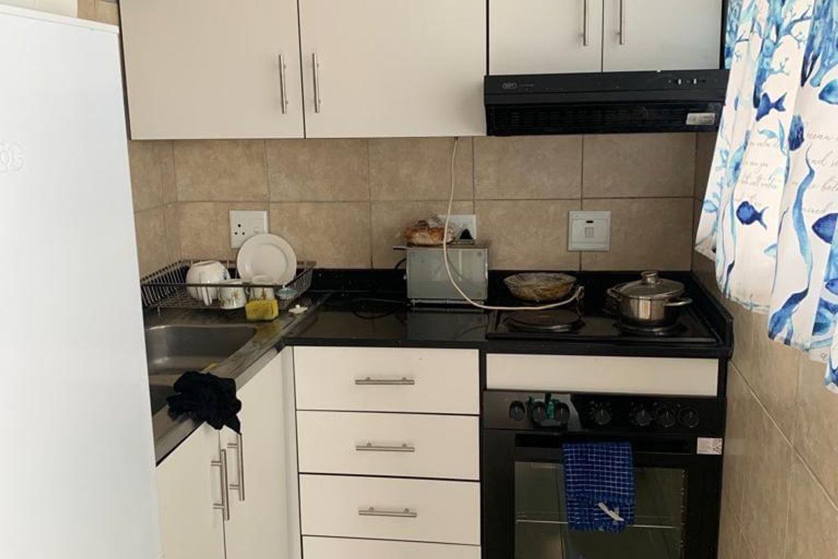 Compact kitchen featuring white cabinetry, black countertops, built-in oven and hob, and tiled finishes. Requires minor repairs to wall tiling.