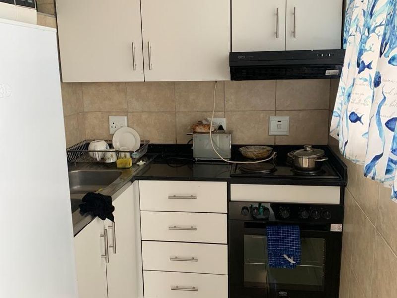 Compact kitchen featuring white cabinetry, black countertops, built-in oven and hob, and tiled finishes. Requires minor repairs to wall tiling.