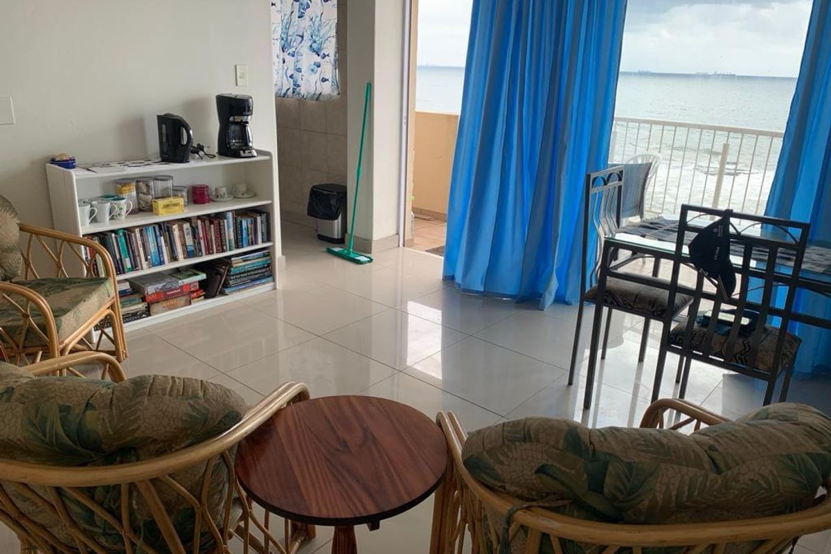 A bright living area featuring tiled flooring and direct access to a balcony with ocean views through a large sliding glass door.