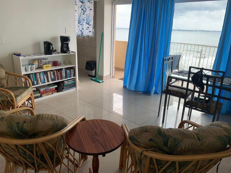 A bright living area featuring tiled flooring and direct access to a balcony with ocean views through a large sliding glass door.