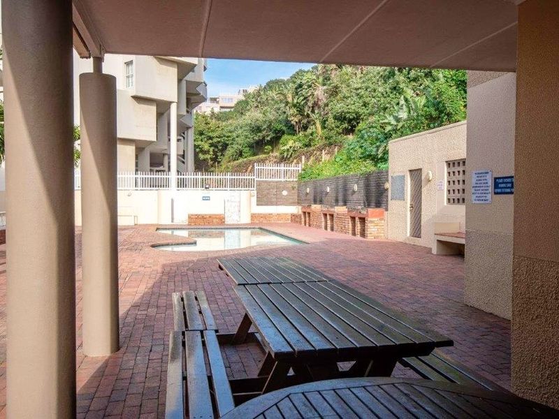 Communal pool area featuring brick paving, a covered patio space, and surrounding boundary walls within the apartment complex.