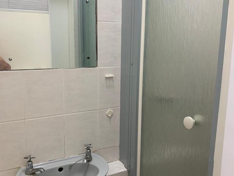 A compact bathroom featuring a wall-mounted basin, tiled splashback, and a shower enclosure with a textured glass door.