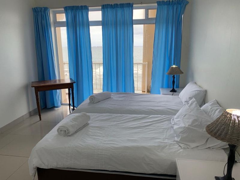 A bedroom featuring tiled flooring and a large sliding glass door providing direct access to a balcony with ocean views.