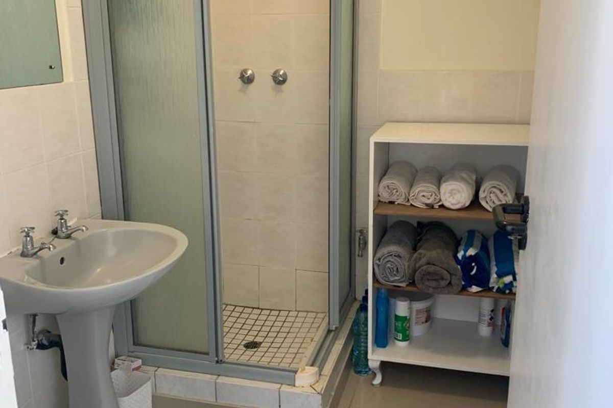 A functional bathroom featuring a pedestal basin, a corner shower enclosure, and a standard toilet with neutral wall and floor tiling.