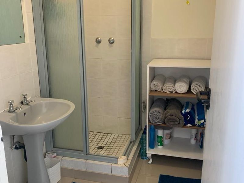A functional bathroom featuring a pedestal basin, a corner shower enclosure, and a standard toilet with neutral wall and floor tiling.
