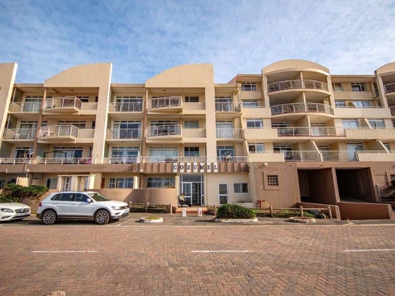 Front elevation of the Cozumel apartment complex, featuring multi-level balconies, paved parking area, and secure building entrance.