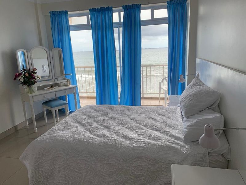 A bedroom featuring tiled flooring and large sliding glass doors that open onto a balcony with direct ocean views.