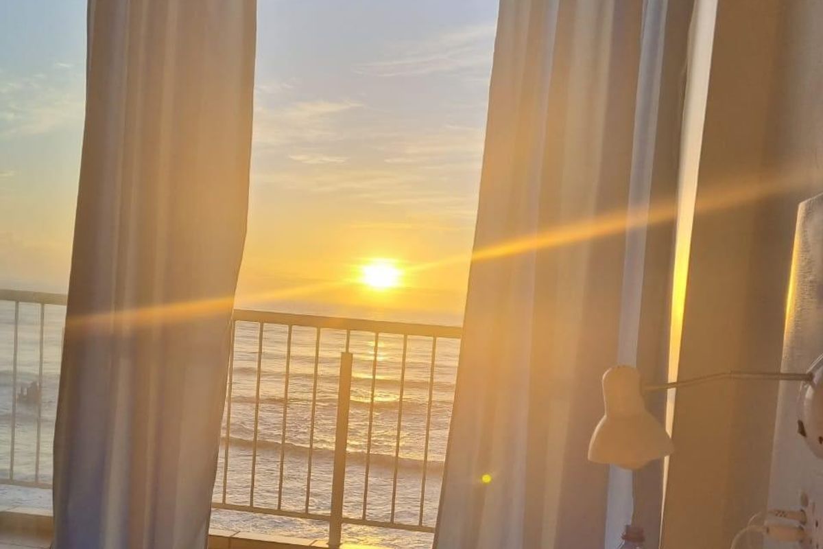 Bedroom featuring a sliding glass door that opens onto a balcony with a scenic ocean view at sunset.