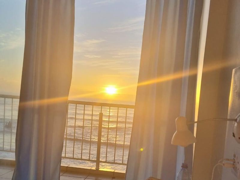 Bedroom featuring a sliding glass door that opens onto a balcony with a scenic ocean view at sunset.