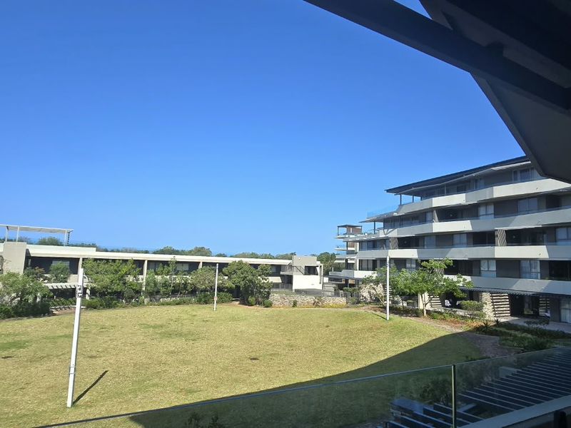 Elevated view overlooking a well-maintained communal lawn and modern apartment building architecture from a private balcony.