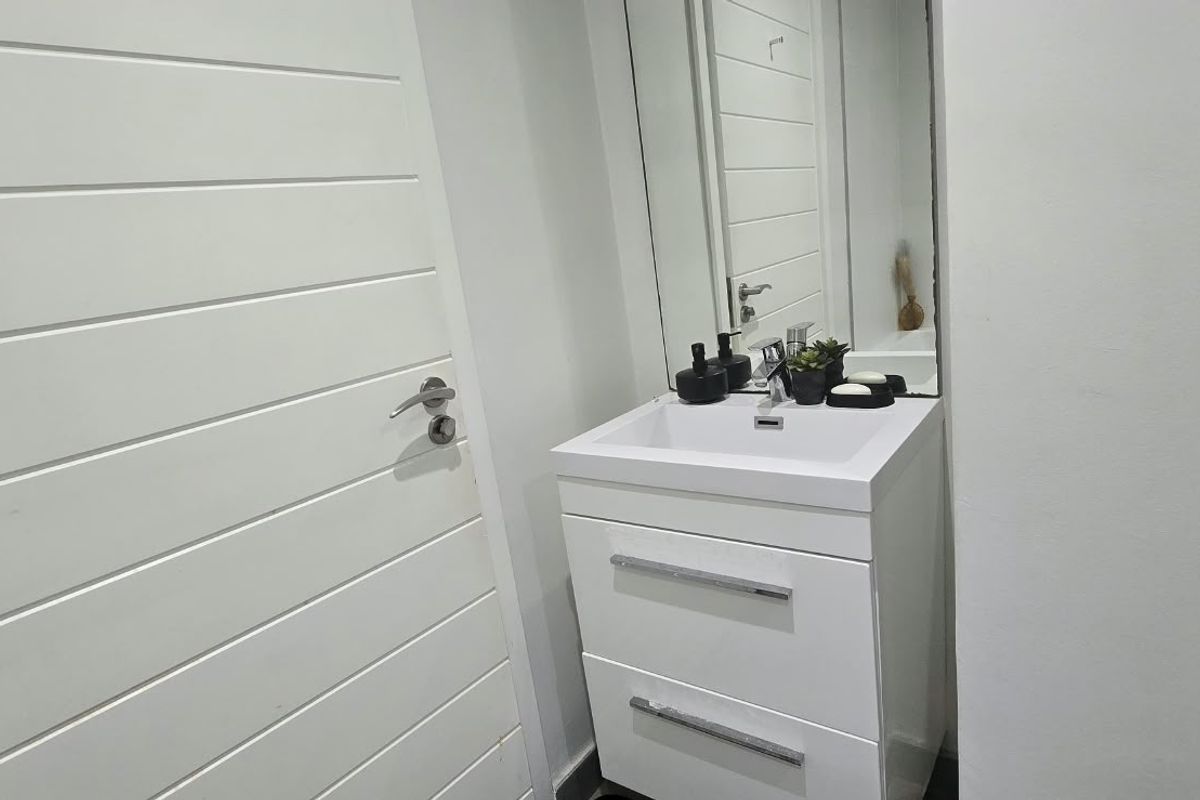 A clean and modern bathroom featuring a white vanity cabinet with a basin, mixer tap, and a large wall-mounted mirror.